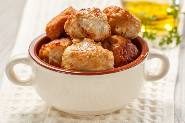 Costeletas de carne frita na tigela de sopa de cerâmica e garrafa com óleo de girassol no pano de prato branco.