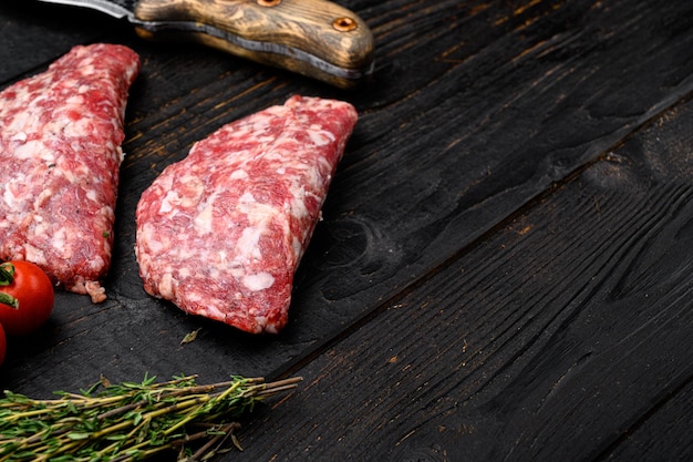 Costeletas de carne picada crua em fundo de mesa de madeira preta com espaço de cópia para texto