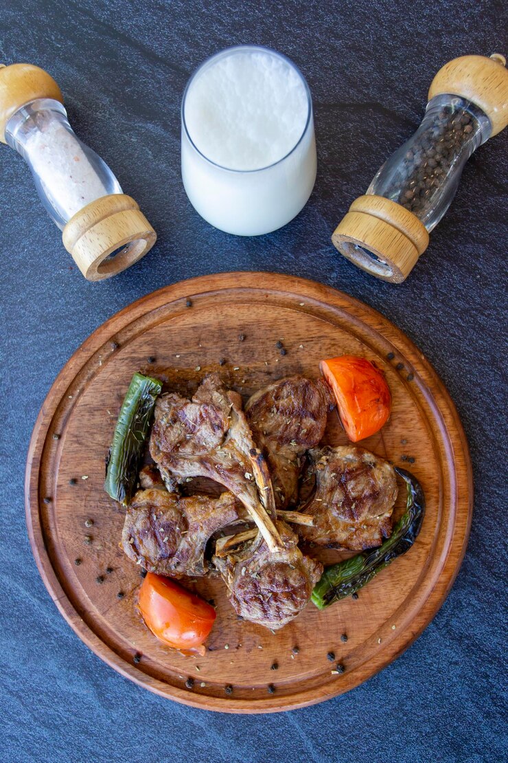 Foto costeletas de cordeiro de churrasco em fundo de madeira com pimentão assado, tomate e cebola