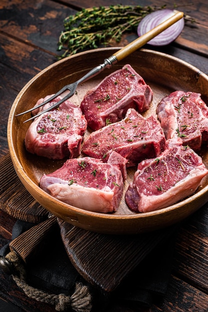 Costeletas de lombo de cordeiro cru bifes em placa de madeira com ervas fundo de madeira vista superior