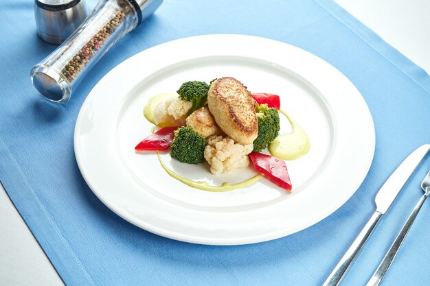 Costeletas de peru da dieta guarnecidas com legumes cozidos no vapor em um prato branco sobre uma toalha de mesa azul.