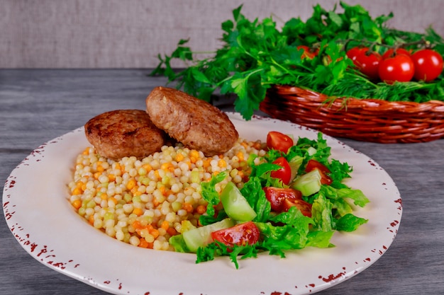 Costeletas de porco, cuscuz com legumes e rúcula.