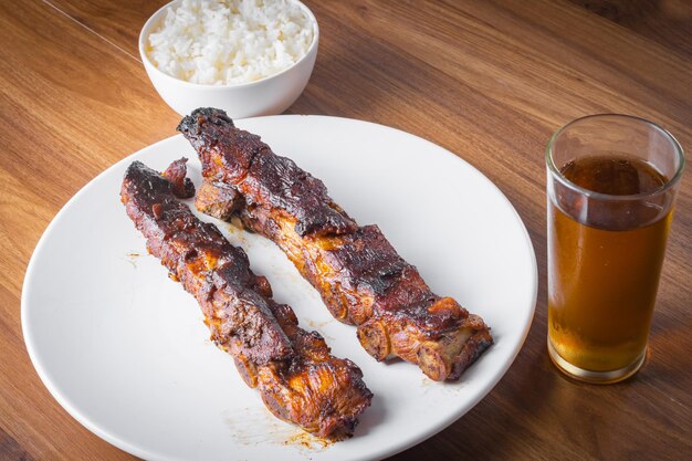 Costelinha de porco assada com arroz ao molho barbecue e refrigerante de guaraná em prato de porcelana branca Mesa de madeira