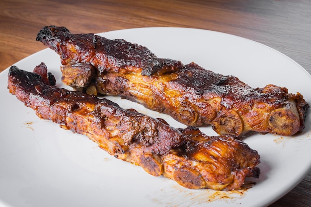 Costelinha de porco assada com molho barbecue em prato de porcelana branca com grafite e faca Mesa de madeira