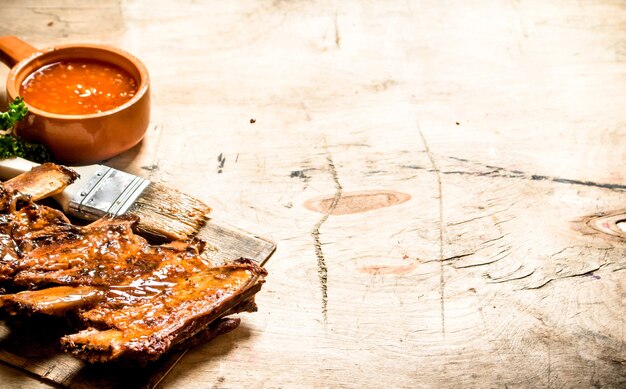 Costelinha de porco defumada com molho picante e um pincel na mesa de madeira.