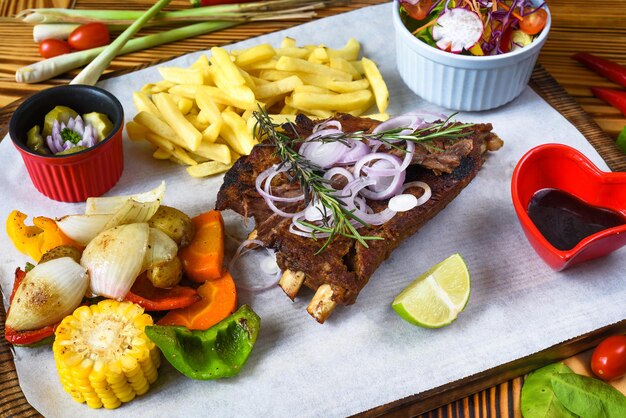 Foto costelinha de porco defumada grelhada com batatas fritas e molho de soja e salada na tábua de madeira