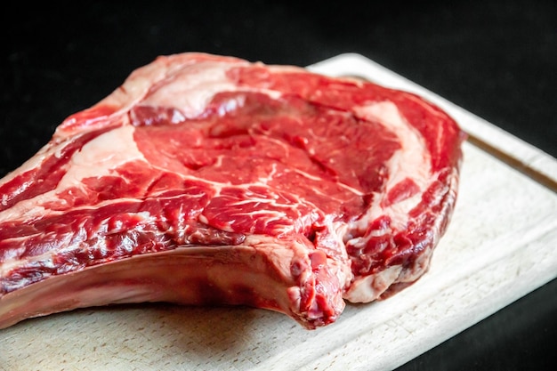 Costilla de ternera cruda sobre una tabla de cortar aislada sobre fondo negro