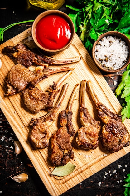 Costillar de cordero a la parrilla sobre una tabla de cortar con perejil y salsa de tomate