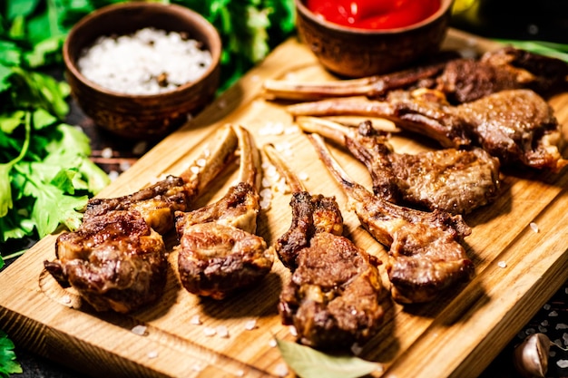 Costillar de cordero a la parrilla sobre una tabla de cortar con perejil y salsa de tomate