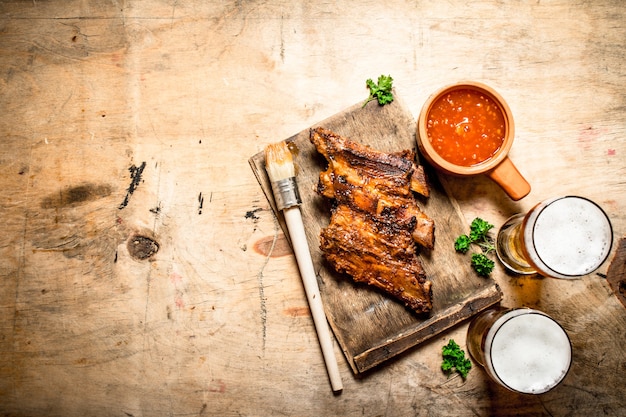 Costillas ahumadas a la barbacoa con salsa de tomate y cerveza fría. Sobre mesa de madera.