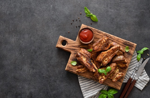 Costillas ahumadas a la parrilla sobre una tabla de madera con salsa y albahaca sobre una mesa de piedra