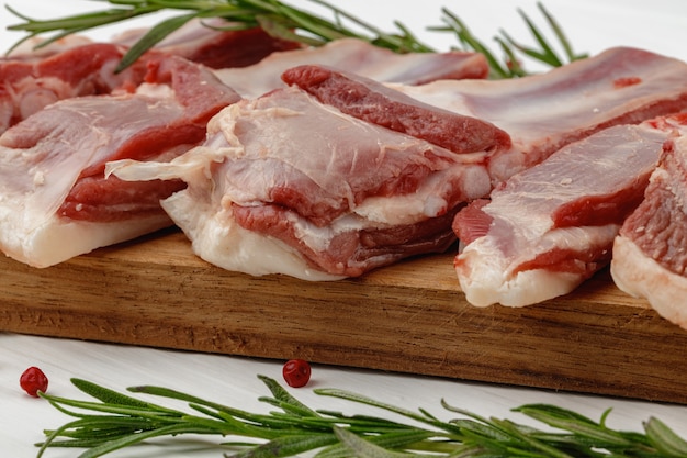 Costillas de carne cruda sobre tabla de madera sobre fondo blanco.