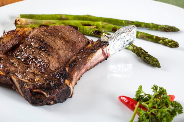 Costillas de carne a la parrilla en un plato blanco con tomate cebollino y salsa picante oscura a bordo