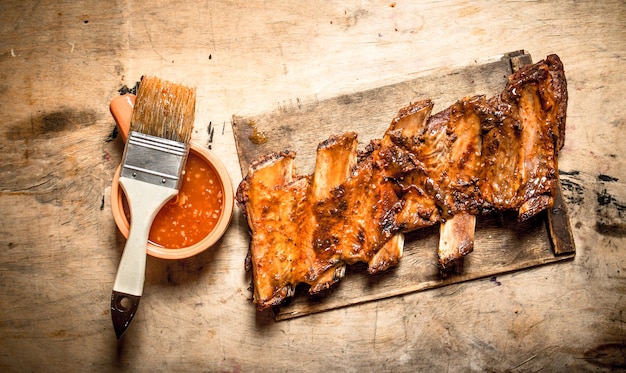 Costillas de cerdo ahumadas con salsa picante y un pincel sobre mesa de madera.