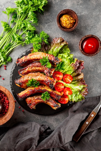 Costillas de cerdo al horno con verduras, mostaza y salsa de tomate sobre fondo gris, vista superior, foto vertical