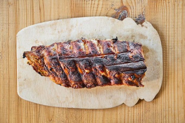 Costillas de cerdo asadas a la parrilla sobre una tabla de servir de madera sobre un fondo de mesa de madera. Vista superior.