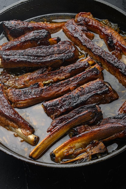 Costillas de cerdo asadas con salsa BBQ y caramelizadas en miel, en sartén de hierro fundido, sobre fondo de piedra negra