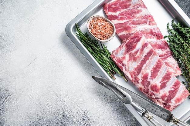 Costillas de cerdo cruda en bandeja de cocina con hierbas