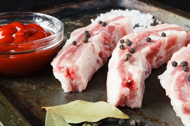 Costillas de cerdo crudas en bandeja de acero con ingredientes