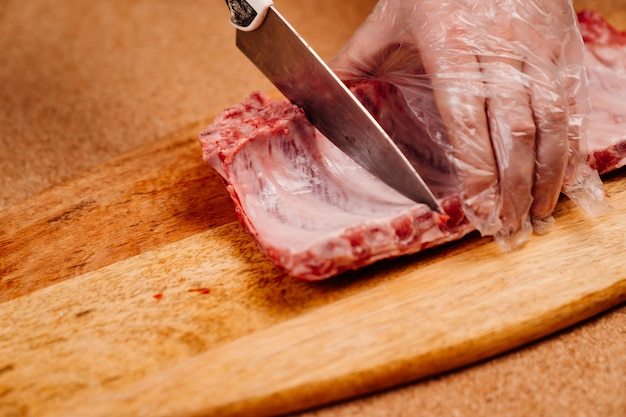 Las costillas de cerdo crudas se cortan con un cuchillo sobre una tabla de cortar de madera.