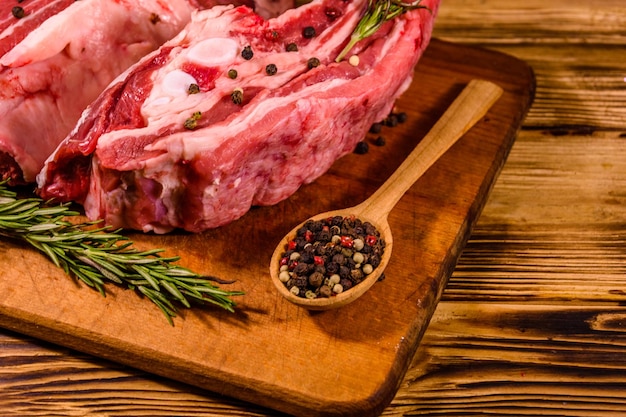 Foto costillas de cerdo crudas con especias y romero sobre una tabla para cortar