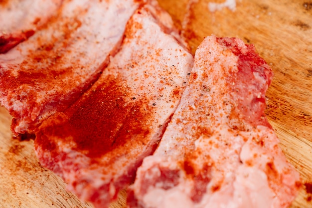 Costillas de cerdo crudas espolvoreadas con sal, pimienta negra y pimentón sobre una tabla de cortar de madera.