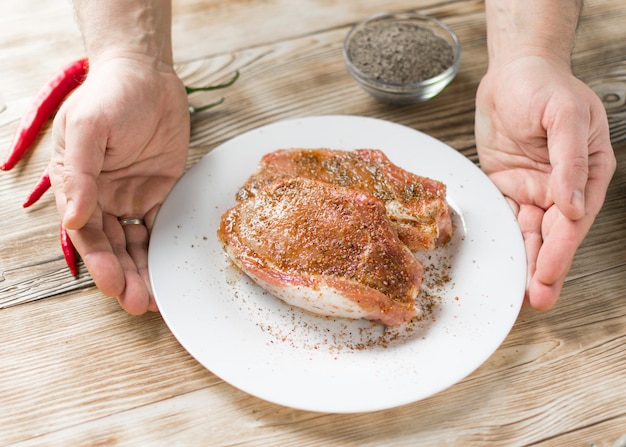 Costillas de cerdo crudas con pimiento rojo picante La mano de un hombre sostiene un plato