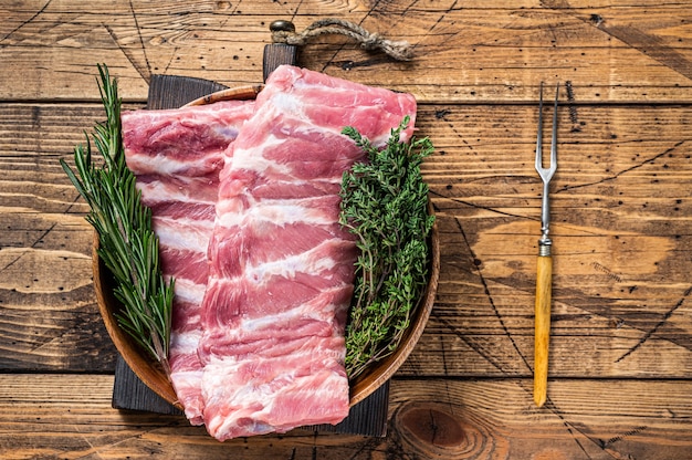 Costillas de cerdo crudas en placa de madera con horquilla de carne