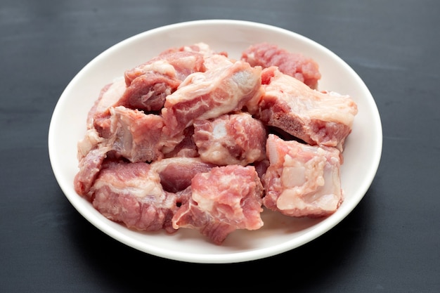 Costillas de cerdo crudas en plato blanco sobre fondo oscuro.