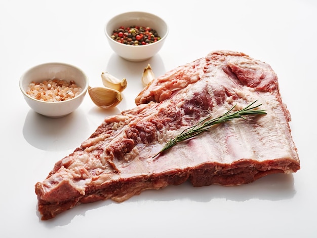 Costillas de cerdo crudas sobre fondo blanco con especias y romero