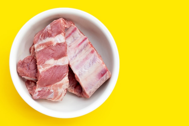 Costillas de cerdo crudas en un tazón blanco sobre fondo amarillo.