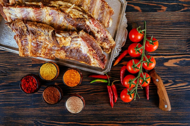 Costillas de cerdo marinadas crudas y tomates de pimienta de ajo en un tablero negro