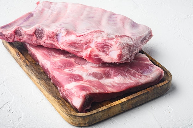 Foto costillas de cerdo orgánicas en una tabla de servir de madera sobre fondo de piedra blanca