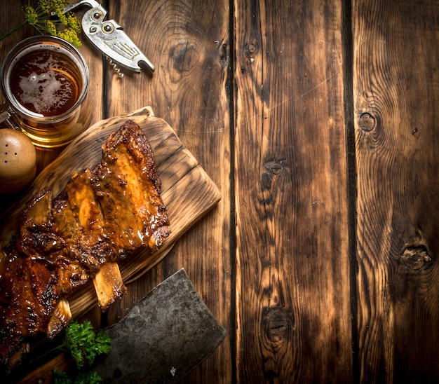 Costillas de cerdo a la parrilla con un hacha de carne y cerveza en la mesa de madera.