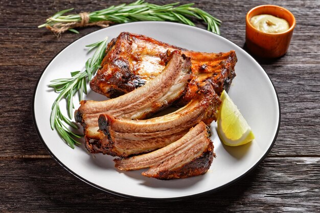 Costillas de cerdo a la parrilla con limón y romero en un plato sobre una mesa de madera oscura con vista horizontal de ketchup y mostaza desde arriba