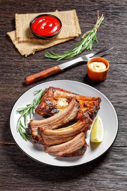 Costillas de cerdo a la parrilla con limón y romero en un plato sobre una mesa de madera oscura con vista vertical de ketchup y mostaza desde arriba