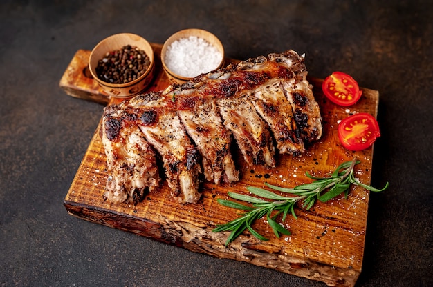 Costillas de cerdo a la parrilla sobre una tabla de cortar con especias sobre un fondo de piedra