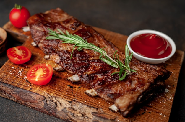 Foto costillas de cerdo a la parrilla sobre una tabla de cortar con especias sobre un fondo de piedra