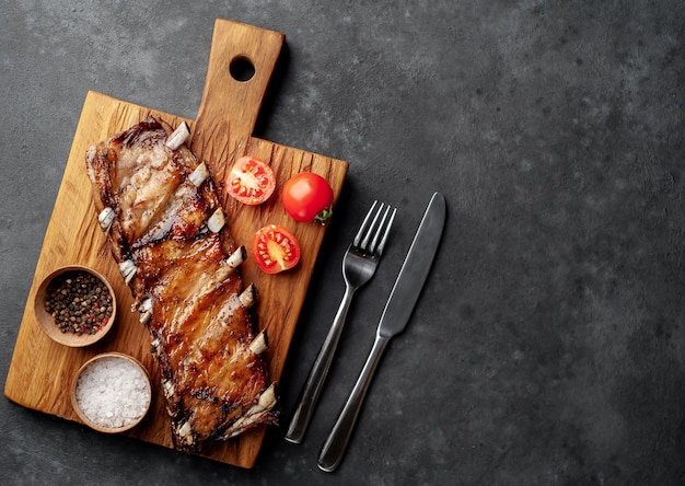 Costillas de cerdo a la parrilla sobre una tabla de cortar con especias sobre un fondo de piedra