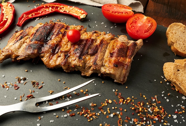 Costillas de cerdo a la parrilla en un tablero negro, tomates rojos frescos