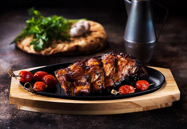 Costillas de cerdo a la parrilla y tomates al horno en una tabla para servir