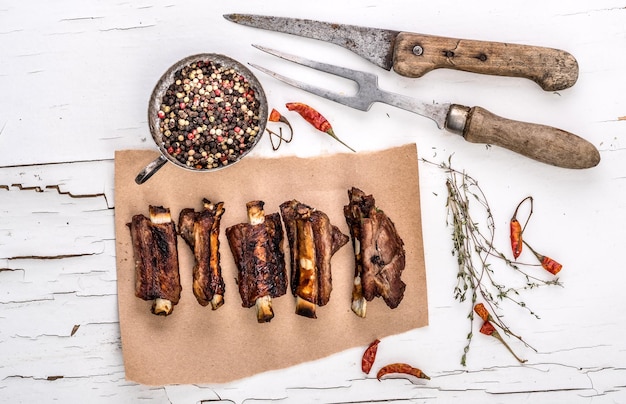 Costillas de cerdo a la parrilla en un trozo de papel marrón con especias de hierbas y tenedor tallado en una mesa de madera blanca con