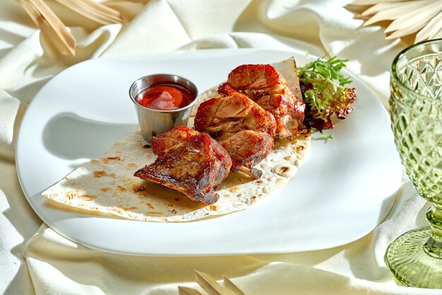 Costillas de cerdo a la plancha con pan de pita y salsa roja. Costillas BBQ en un plato blanco.