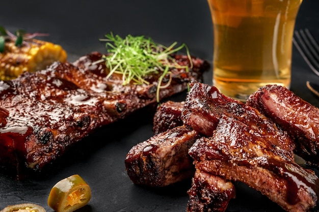 Costillas de cerdo en salsa barbacoa y un vaso de cerveza en un plato de pizarra negra Un gran bocadillo para la cerveza en un fondo de piedra oscura Vista superior con espacio para copiar