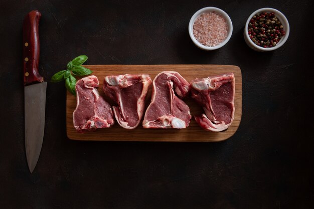 Costillas y condimentos frescos crudos de la carne del cordero en fondo de madera oscuro