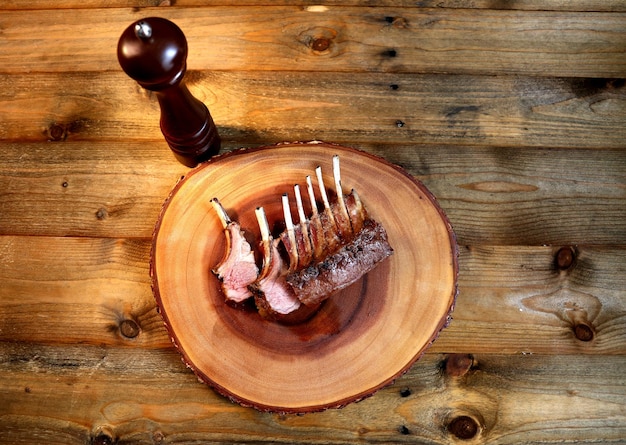 Costillas de cordero francés a la parrilla en la barbacoa en un fondo de madera con un cuchillo pequeño, sal y pimienta