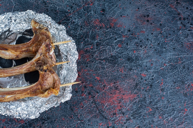 Costillas de cordero a la plancha con palos colocados sobre mesa de mármol.