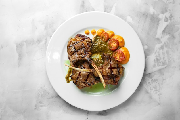 Costillas de cordero a la plancha sobre tabla de cortar con verduras asadas. De cerca.