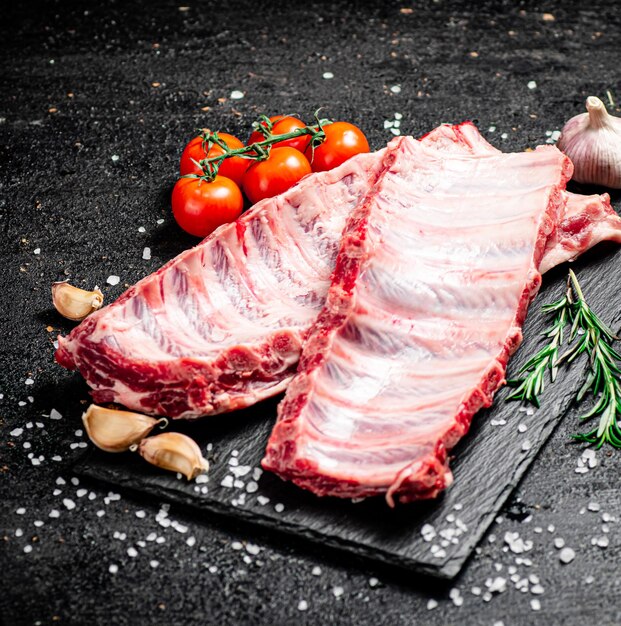 Costillas crudas sobre una placa de piedra con tomates y trozos de sal