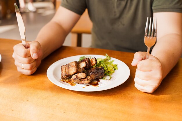 Foto costillas a la parrilla con ensalada en un plato blanco sobre una mesa de madera